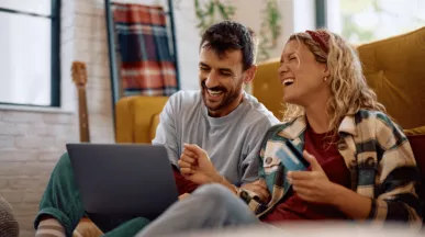 Szczęśliwa para siedzi na podłodze, przeglądając promocje na laptopie i trzymając kartę podarunkową, co pokazuje, co motywuje klientów do zakupu.