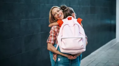Uśmiechnięta matka przytula córkę w różowym plecaku szkolnym przed rozpoczęciem roku szkolnego